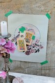 Zarte Collage mit nostalgischen Motiven an Betonwand mit Masking Tape fixiert; Silberne Kerzenhalter mit Hortensienblüten