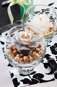Candle lanterns with flower-shaped candles on wooden beads on black and white place mat