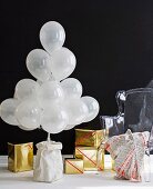 Stylised Christmas tree made from white balloons and presents wrapped in gold paper against black background