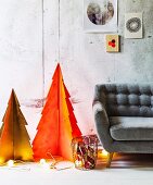 Two stylised cardboard Christmas trees sprayed orange and gold, lit fairy lights on floor and grey retro sofa