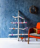 Stilisierter Weihnachtsbaum aus Strandgut gezimmert mit Weihnachtsanhängern geschmückt an blauer Wand und Dekopilzen am Boden