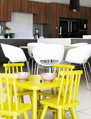 Yellow children's table and chairs in front of modern, white shell chairs in open-plan kitchen