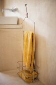 Gelbe Handtücher in Vintage Metallkorb mit Haken vor hellgrauer Betonwand, dahinter weisses Waschbecken auf gemauertem Unterbau und Wandarmatur
