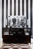 Black, half-height hifi cabinet with flatscreen TV against wall with elegant, black and white striped wallpaper