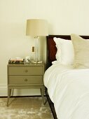 Table lamp on grey-painted bedside cabinet on shimmering rug next to bed with white bed linen
