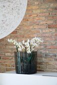 Orchids in smoked glass vase against brick wall; detail of spherical lampshade