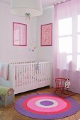 Nursery with framed, patterned pictures over white cot; rocking horse on round rug in shades of lilac and pink