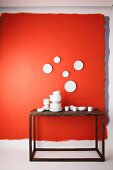 Stacks of white china crockery on wooden table below plates hung on red wall