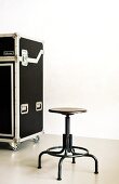 Black swivel stool and transport case on castors in front of patinated wall