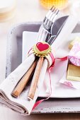 Cutlery and linen napkin in simple napkin ring lovingly decorated with gold bottle cap and heart motif