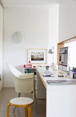 Minimalist, narrow office with white Lord Yo shell chair and yellow-painted wooden stool at modern desk below hatch in wall