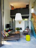 Designer sofas in open-plan, double-height living area with staircase leading to gallery bridge