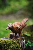 Vogelfigur aus angerostetem Metall auf bemoostem Holzstamm