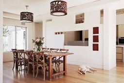 Partition wall with irregular apertures leading to kitchen; dining area with wooden chairs and floral lampshades