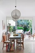 Vintage dining table and bamboo chairs below pendant lamps with spherical mesh lampshades and view of outdoor furniture and garden through open terrace doors