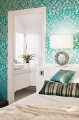 Partially visible bed in bedroom with patterned wallpaper and view into ensuite bathroom through open door