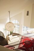 View down into living area with Oriental rug, modern, white chaise longue & spherical pendant lamp