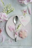 Herzförmiger Namensschild, Rosenblütenplätzchen und Löffel mit Maiglöckchen auf Teller