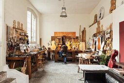 Geigenbauer in seiner Werkstatt mit verschiedenen Werkbänken und Werkzeugen