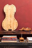 Stack of books, tuning fork, wooden shoe lasts and pale cello body leaning against dark red wall on rustic wooden surface