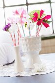Zwei weiße Porzellanvasen im Retrostil mit Sommerblüten und Trinkhalmen