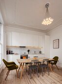 Simple, white fitted kitchen in renovated period apartment with wooden floor, retro-style dining area and designer pendant lamp hanging from ceiling with stucco frieze