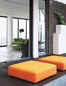 Orange ottomans on dark wooden terrace with view into living area of loft apartment through open sliding glass wall