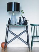 Table lamp with black lampshade next to collection of vases on rustic, metal console table