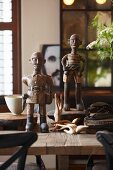 Zwei geschnitzte kahlköpfige Männerfiguren mit anderen kunsthandwerklichen Holzobjekten auf rustikalem Holztisch in Vintage-Wohnambiente