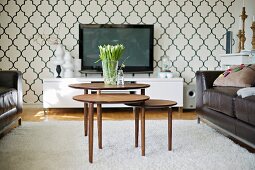 Nest of 50s tables, black leather sofas and modern media centre against wallpaper with stylised azulejo pattern