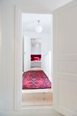 View through open interior doors along corridor with Oriental rug, spherical lamp and bedroom at far end