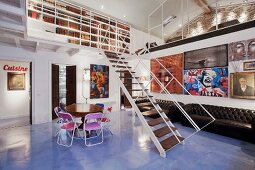 Luftiger Wohnraum mit filigraner Galerie Stahltreppe und zwei dunklen Ledersofas vor Wand mit Bildergalerie