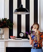 Woman arranging bouquet of hyacinths on mantelpiece against wallpaper with wide black and white stripes