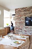 Set dining table in front of TV on old brick wall with view of open-plan kitchen in background