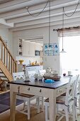 Rustic dining table and white wooden chairs in open-plan interior with maritime character