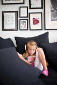 Little girl listening to music amongst black cushions in front of collection of black-framed pictures