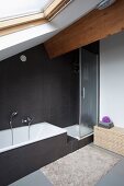 Designerbad unter dem Dach mit eingebauter Badewanne und Duschkabine vor schwarzen Fliesen an Wand