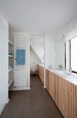 Modern bathroom; fitted cupboards with vertical slatted doors and integrated sink below window, white towel warmer on wall next to sliding door