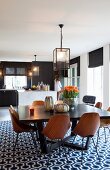 Wooden shell chairs with metal frames around dark dining table on retro rug with geometric patter in spacious interior with open-plan kitchen