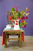 Autumnal branches of viburnum berries in enamel jug on rustic chair