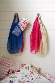 Net shopping bags of different colours hanging on white wall above embroidered scatter cushion