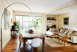 Living-dining room with classic, designer pieces, arc lamp over rustic wooden tables and 50s laminated wood furniture in front of corner sofa