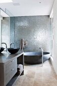 Designer bathroom with round bathtub against wall with grey, shimmering structure and washstand with anthracite basin