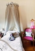 Rag doll on child's fairy-tale bed with crown-shaped canopy next to antique chair with deep pink upholstery