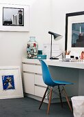 Moderne Kunstsammlung im Homeoffice mit weißem Einbauschreibtisch, blauem Eames Chair und Tischleuchte von Louis Poulsen