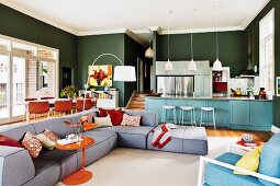Sofalandschaft, Essbereich und Küchentheke in offenem Wohnraum mit grüner Wand