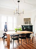 Simple metal chandelier above modern wooden table and black chairs in dining room with marquetry parquet floor and stucco ceiling