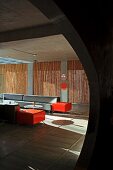 View though rounded opening into minimalist lounge area with grey and orange sofa set; screens of bamboo poles in windows in background