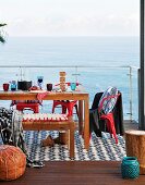 Wooden bench, set table and red retro chairs on terrace with sea view through transparent glass balustrade