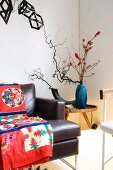 Colourful ethnic blanket on leather sofa, plant arrangement on side table in corner and objets d'art on wall
